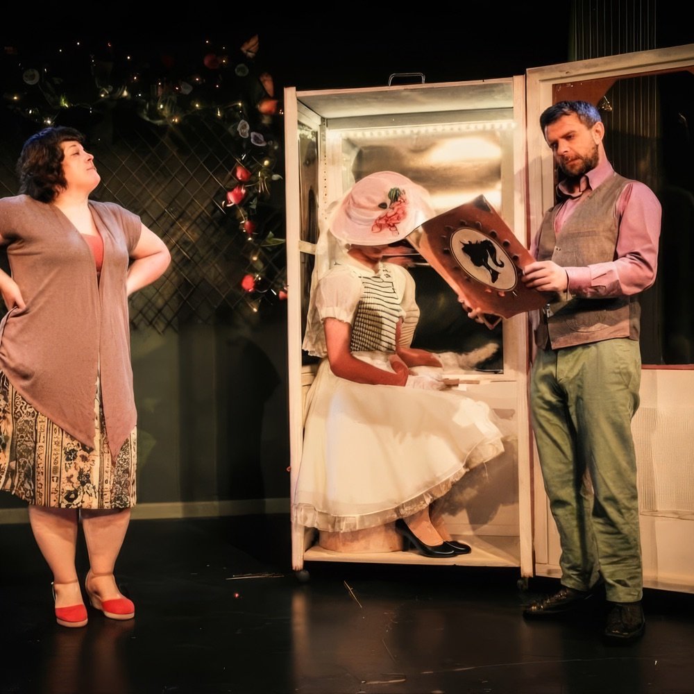 Tres actores en escena junto a un armario iluminado